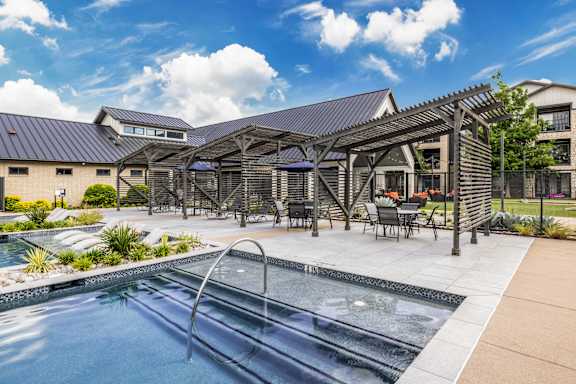 A pool area with a hot tub and a building in the background.
