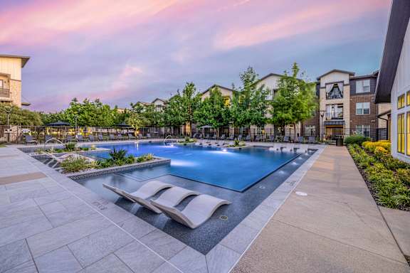 A swimming pool surrounded by a stone patio and lounge chairs.