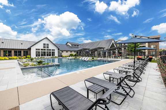 A pool area with sun loungers and a building in the background.