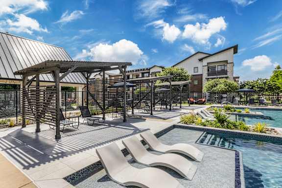 A pool area with a metal pergola and lounge chairs.
