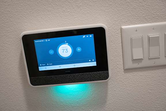 A smart thermostat is mounted on a wall and shows the temperature as 73 degrees.