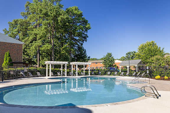 A large swimming pool surrounded by trees and lounge chairs.