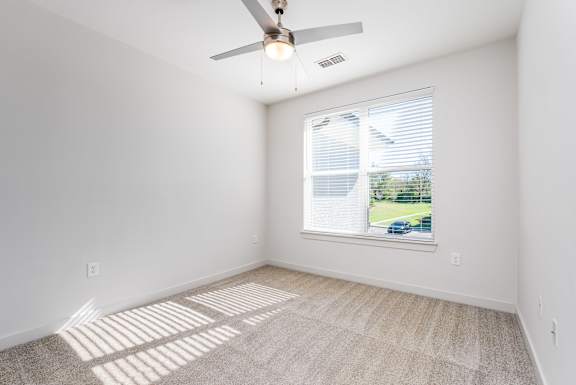 A room with a ceiling fan and a window showing a view of a house and trees outside.