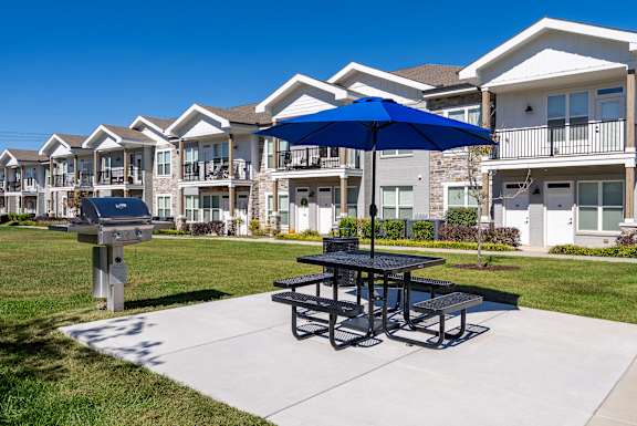 A picnic table with a blue umbrella is in the foreground of a residential area.