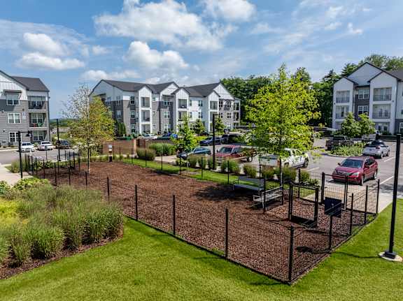 A view of a landscaped area with a fence and apartment buildings in the background.