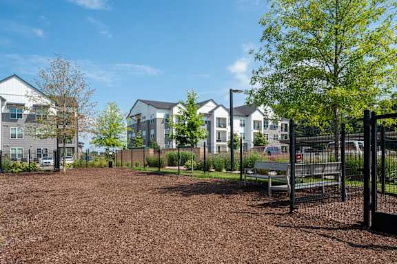 A playground area with a bench and a fence in front of a residential area.