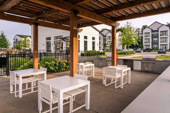 A patio with white chairs and tables under a wooden pergola.