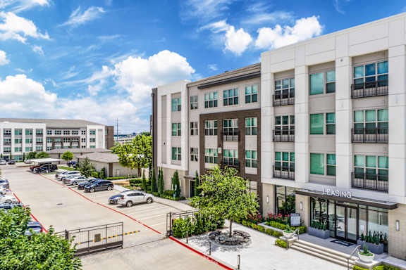 A parking lot in front of a multi-story building with a sign that says "Leasing.".