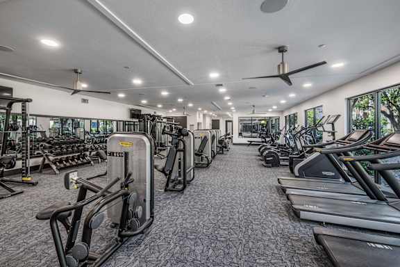 A gym with a variety of equipment including treadmills, elliptical machines, and a fan.