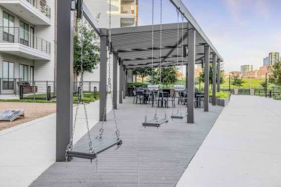 A playground with swings and a canopy is situated in a courtyard.