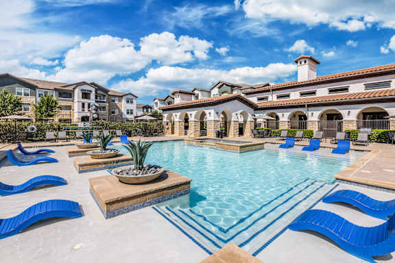 A large swimming pool with blue loungers and a building in the background.