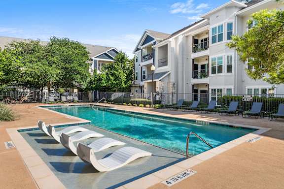 A pool with lounge chairs and a building in the background.