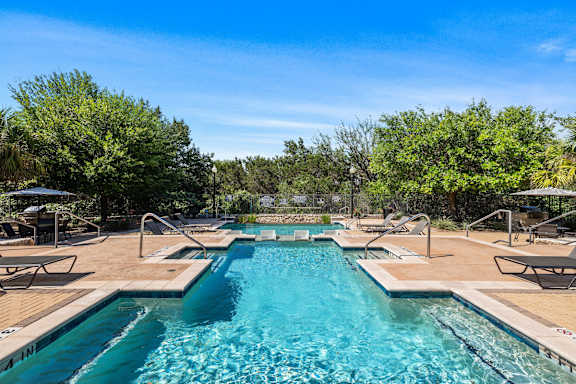 A large outdoor swimming pool surrounded by trees and lounge chairs.