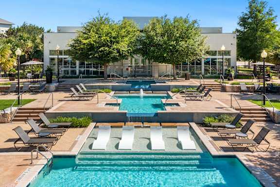 A large swimming pool with lounge chairs and a building in the background.