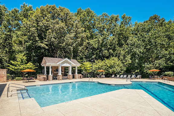 A pool surrounded by trees and a gazebo.
