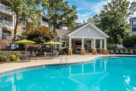 A swimming pool surrounded by chairs and umbrellas with a house in the background.