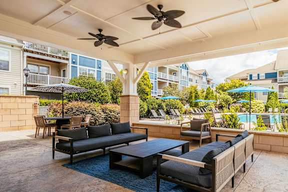 A patio with a couch, chairs, and a table with a fan overhead.