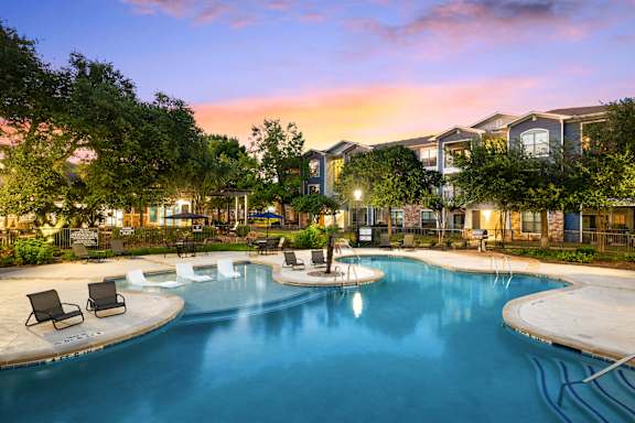 A large swimming pool surrounded by lounge chairs and trees.