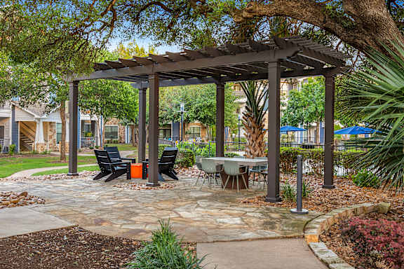 A gazebo with a table and chairs is surrounded by plants and trees.