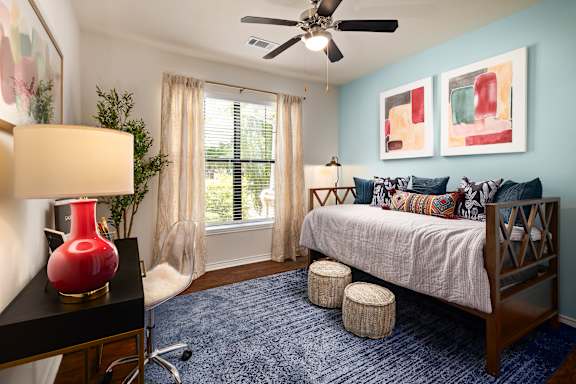 A bedroom with a bed, a ceiling fan, and a red vase on a table.
