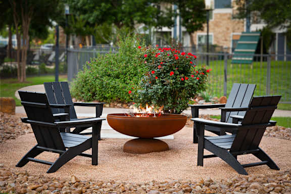 A fire pit surrounded by two chairs and a planter with red flowers.