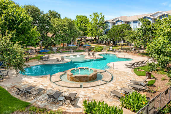 A large outdoor swimming pool surrounded by lawn chairs and trees.