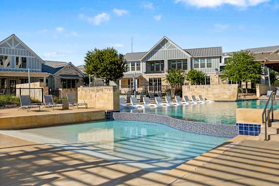 A swimming pool surrounded by lounge chairs and a building in the background.