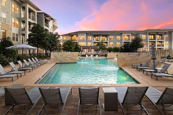 A pool surrounded by chairs and a building in the background.
