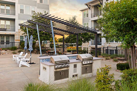 A patio with a grill and chairs under a pergola.