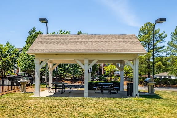 A white pavilion with a brown roof is surrounded by green grass.