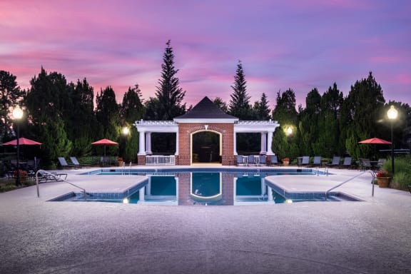 a swimming pool with a brick pool house and a purple sky above it