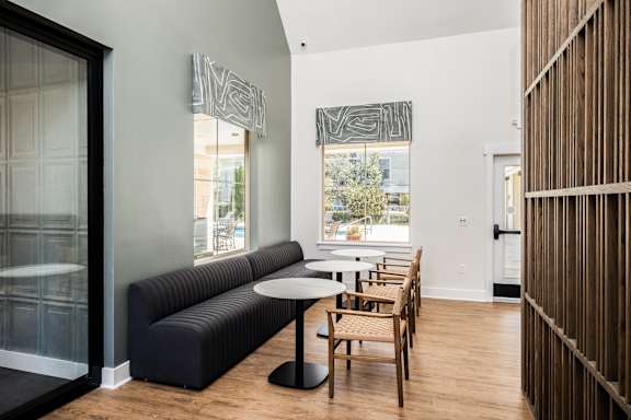 A black sofa with a round table and chairs in front of a window with a view of trees.