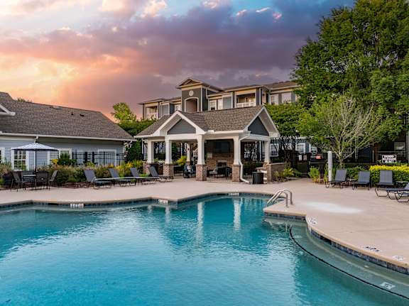 A swimming pool in front of a house with a sunset in the background.