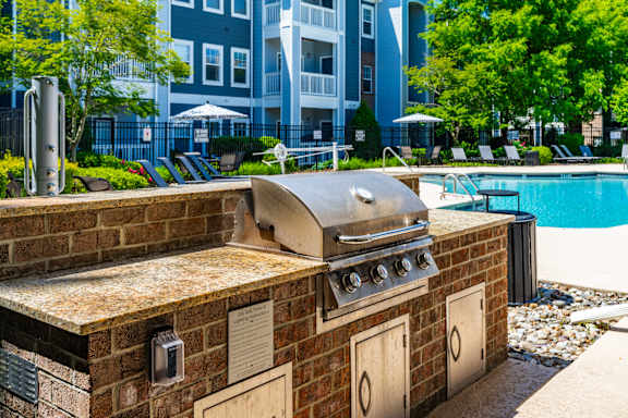 A BBQ grill is on a brick patio next to a pool.