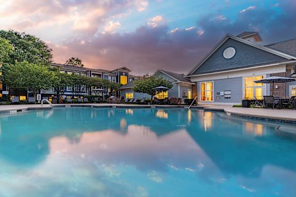 A large swimming pool in front of a house with a sunset sky.