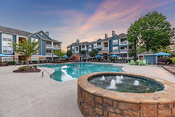 A large outdoor pool with a hot tub in front of apartment buildings.