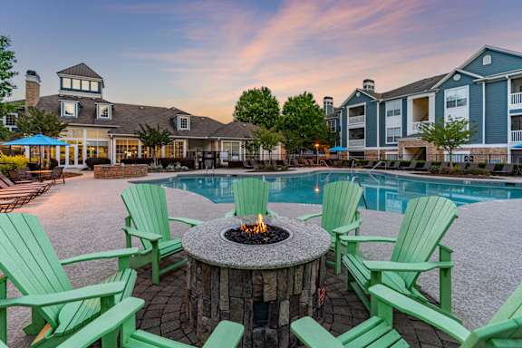 A fire pit surrounded by green chairs sits in the middle of a pool area.