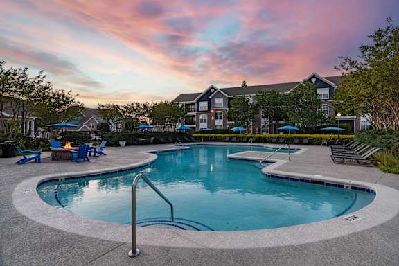 A swimming pool surrounded by a concrete patio and lounge chairs.