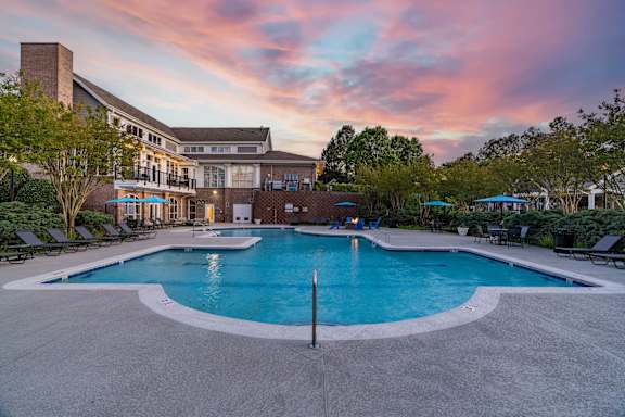 A large outdoor swimming pool surrounded by lounge chairs and trees.