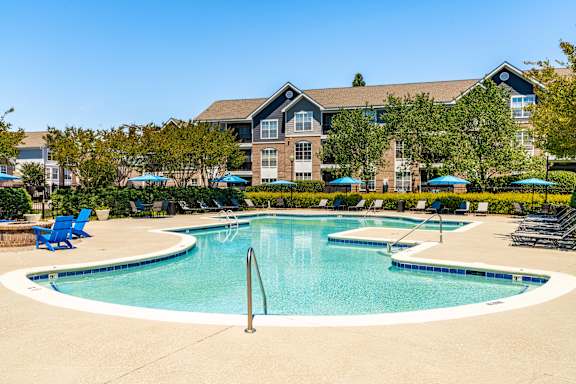 A large swimming pool in front of a building with blue lounge chairs around it.