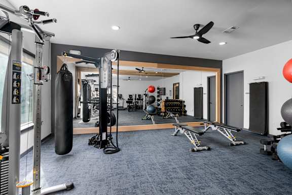 A gym with a variety of equipment including a punching bag, weight bench, and exercise balls.