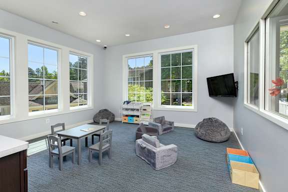 A sunny day outside the windows of a white room with grey carpeting and furniture.