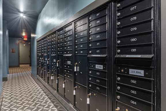 A row of black mailboxes with numbers 077 to 084 are lined up on a tiled floor.