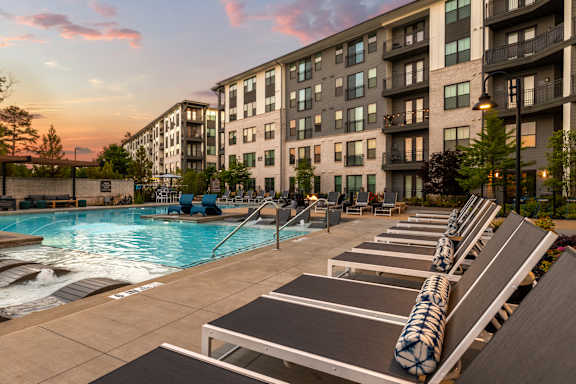 A pool area with sun loungers and apartment buildings in the background.