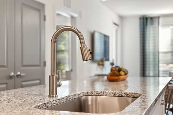A modern kitchen with a stainless steel sink and a gold faucet.