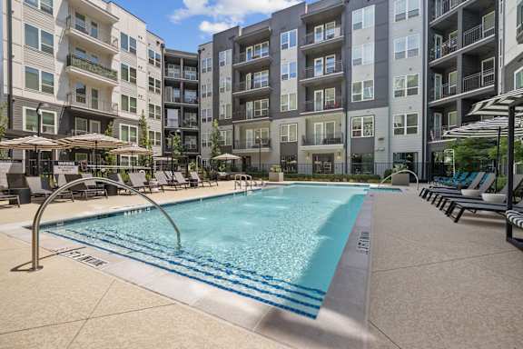 A swimming pool surrounded by apartment buildings and lounge chairs.