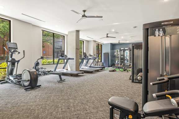 A gym with a variety of equipment including treadmills, weights, and a ceiling fan.