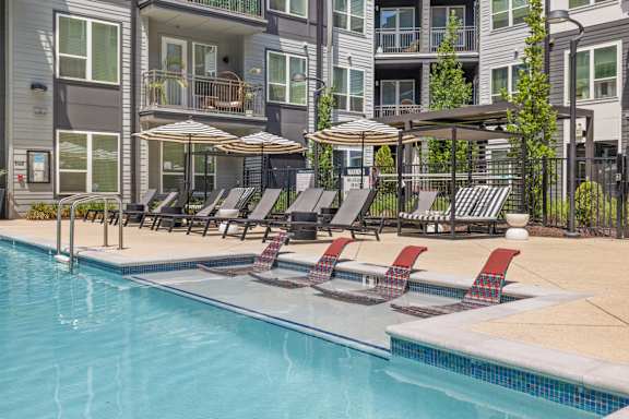 A swimming pool with lounge chairs and umbrellas in front of a building.