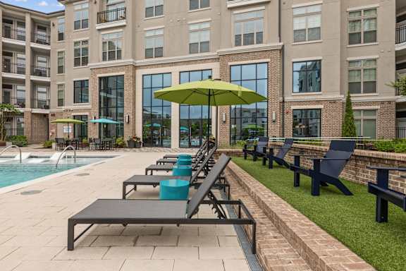 A pool area with a green umbrella and black lounge chairs.