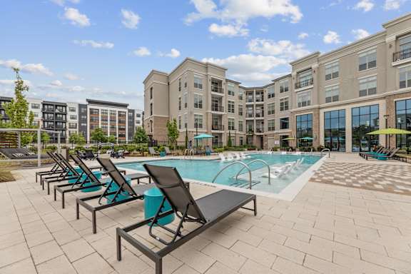 A pool area with lounge chairs and a building in the background.